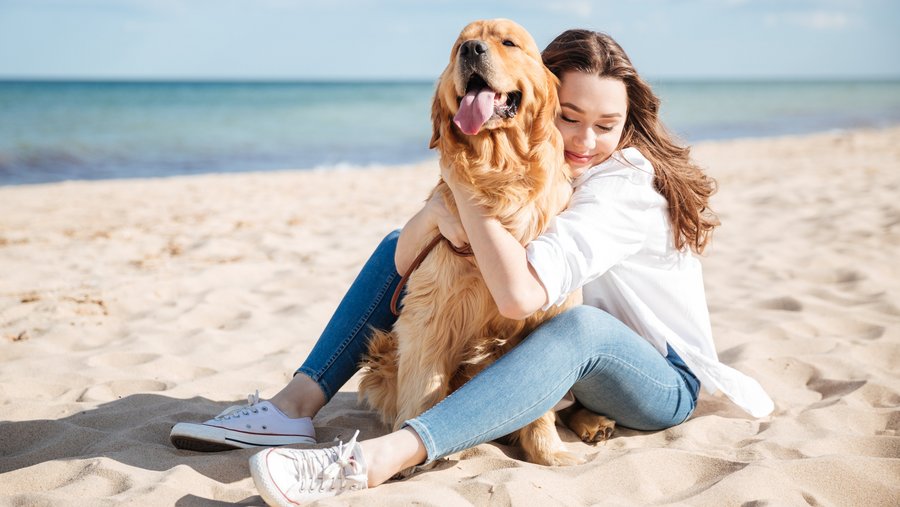 Junge Frau umarmt Golden Retriever am Strand