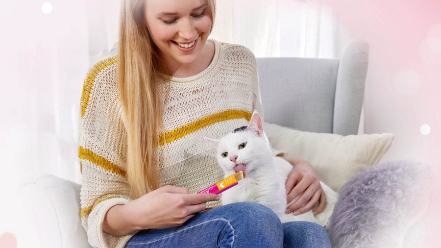 Vrouw heeft kat op schoot en voedt de kat met een Jelly Lovers van Vitakraft