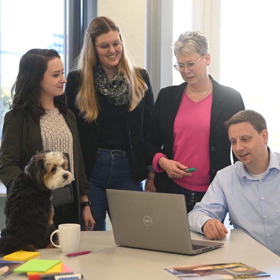 Mitarbeiter schauen zusammen auf Laptop und ein Hund sitzt auf dem Tisch
